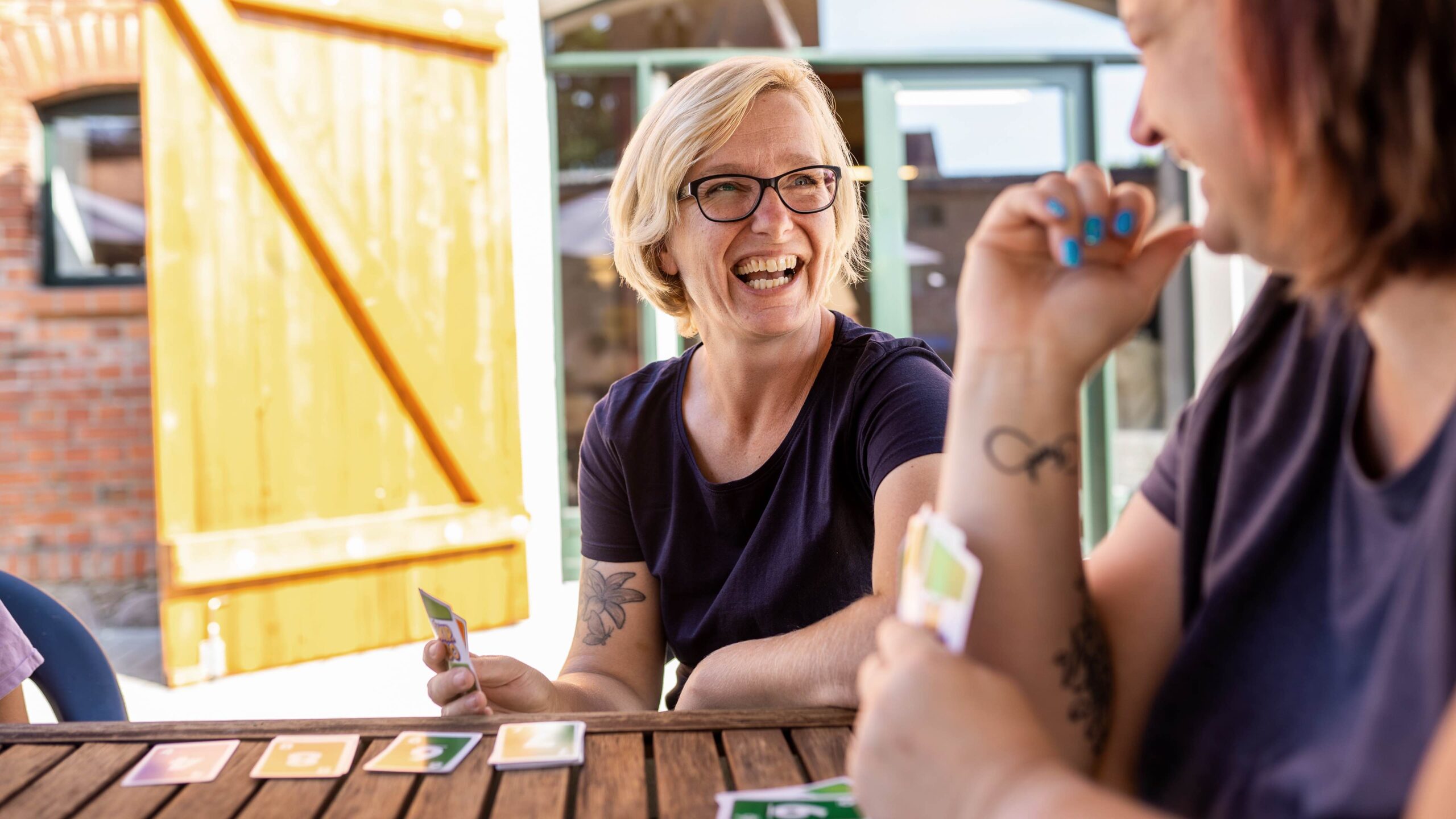 Foto von zwei glücklichen Mitarbeiterinnen des Sozialwerks Winterstein, die Uno an einem Tisch spielen